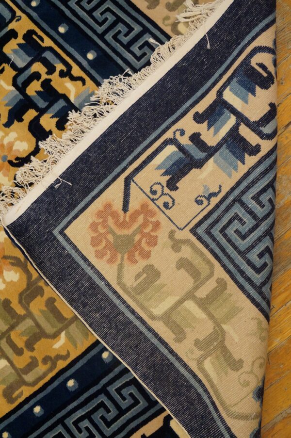 Blue, gold, and tan patterned rug is folded over, revealing the woven backing and fringe on wood flooring.
