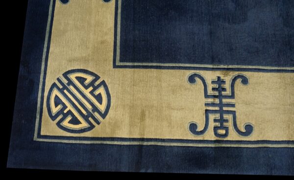A plush navy rug border with a tan band featuring traditional blue and cream geometric and symbolic motifs.