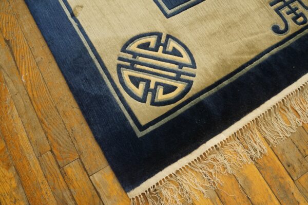 Beige and navy low-pile rug featuring a geometric medallion and fringe over distressed hardwood.
