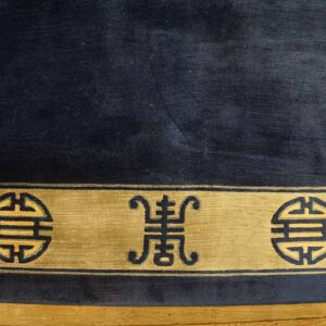Dark blue rug with a gold border featuring repeating geometric symbols rests on wood flooring.