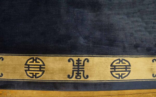Dark blue rug with a gold border featuring repeating geometric symbols rests on wood flooring.