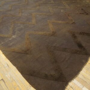 Dark brown rug featuring textured zigzag lines sits on distressed light-colored wood flooring.
