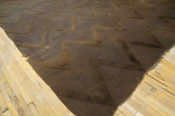 Dark brown rug featuring textured zigzag lines sits on distressed light-colored wood flooring.