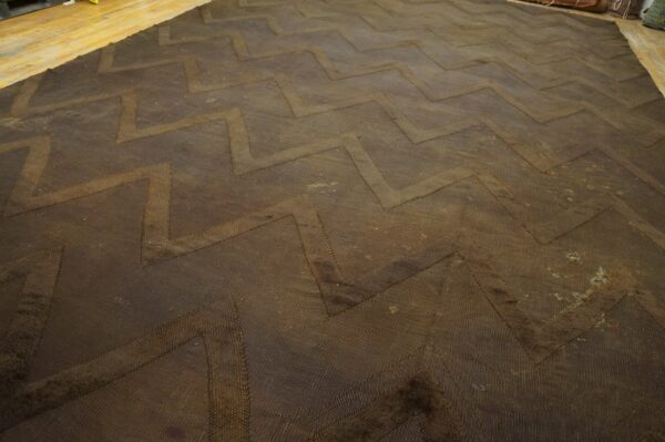 Dark brown textured rug with a repeating zigzag pattern resting on light wooden plank flooring.