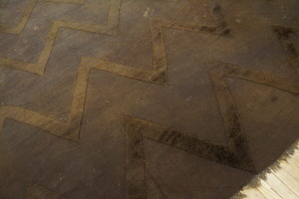 A dark brown rug features a wide chevron pattern in lighter brown textures on visible wood flooring.