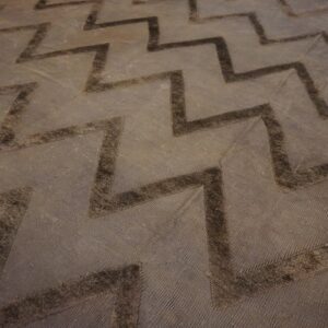 Close-up of a dark brown rug with a raised, tonal chevron pattern over a textured background.