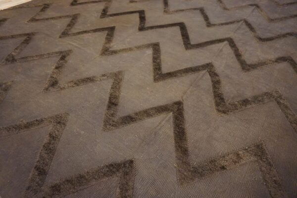 Close-up of a dark brown rug with a raised, tonal chevron pattern over a textured background.