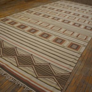 Flatweave rug featuring stripes and geometric patterns in beige, brown, and terracotta on plank wood flooring.