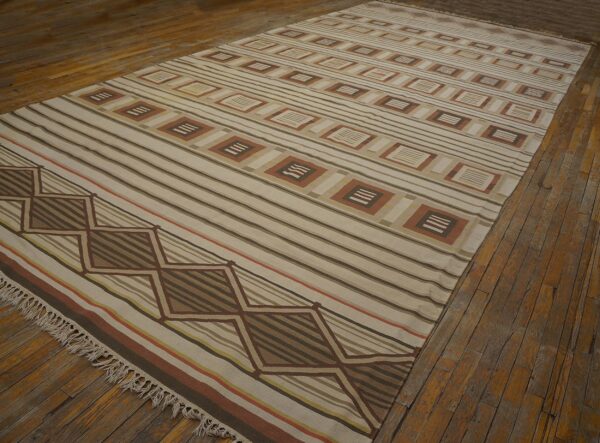 Flatweave rug featuring stripes and geometric patterns in beige, brown, and terracotta on plank wood flooring.