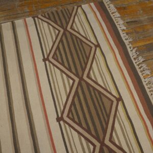 A flatweave rug with earthy stripes and brown zigzag diamonds rests on distressed wooden flooring.