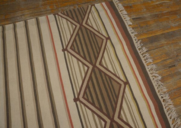 A flatweave rug with earthy stripes and brown zigzag diamonds rests on distressed wooden flooring.