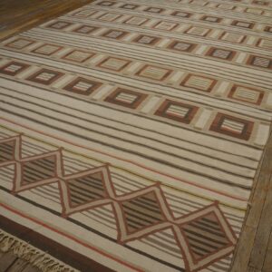 Low pile rug with cream, brown, and terracotta stripes and geometric patterns on a distressed wooden floor.