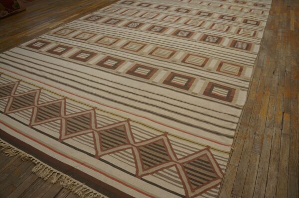 Low pile rug with cream, brown, and terracotta stripes and geometric patterns on a distressed wooden floor.