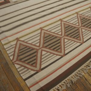 Geometric flatweave rug in neutral browns, ivory, and terracotta stripes, resting on distressed hardwood.