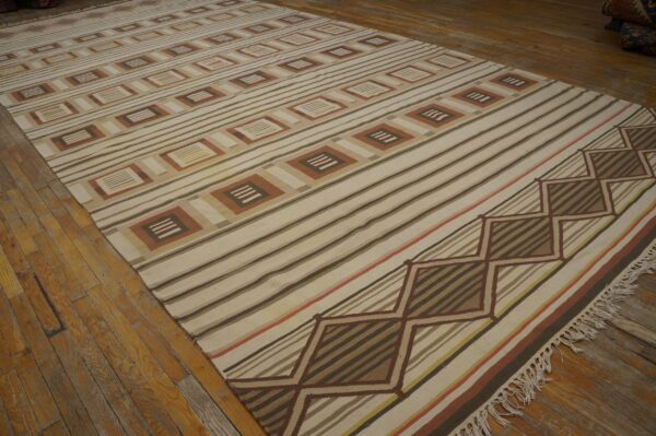 Cream and brown striped flatweave rug with geometric motifs laid on rustic wide plank wood flooring.