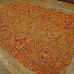 Geometric orange, yellow, and fuchsia rug with a complex, low-texture pattern sits on light wood flooring.