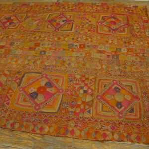 Yellow and orange rug with large embroidered diamond motifs and colorful geometric banding on a worn wood floor.