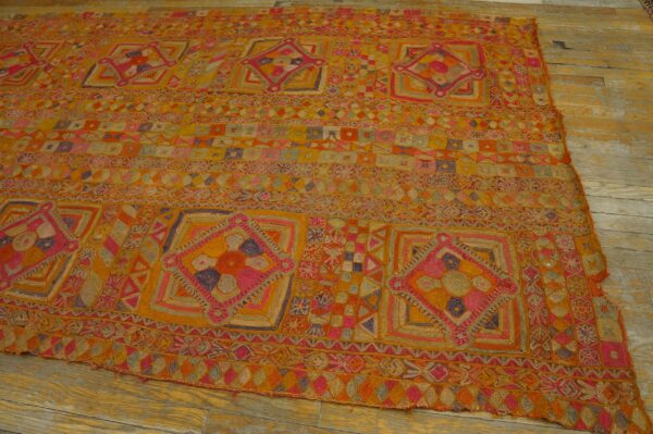 Yellow and orange rug with large embroidered diamond motifs and colorful geometric banding on a worn wood floor.