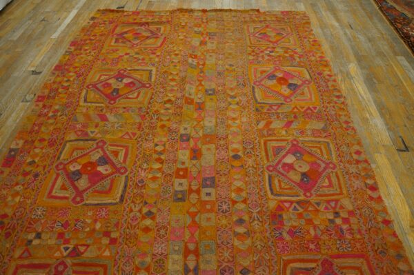 Textured orange and pink rug featuring complex geometric patterns and medallions on distressed wood planks.