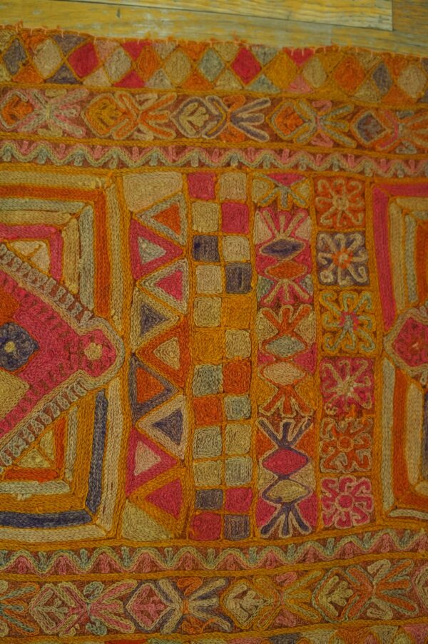 Highly textured rug with bands of pink, orange, and gold geometric motifs resting on wood floorboards.
