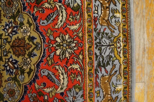 Red, olive, blue, and gold traditional rug detail showing floral patterns, a deer border, and wood flooring.