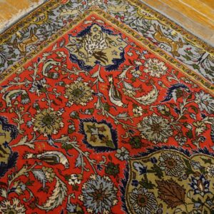 Red floral and animal patterned rug detail rests on shiny distressed hardwood plank flooring.