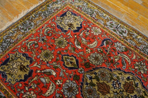 Red floral and animal patterned rug detail rests on shiny distressed hardwood plank flooring.