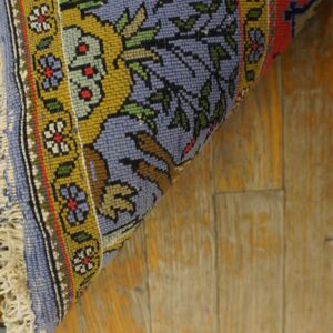 A rolled blue, gold, and red floral patterned rug rests diagonally on distressed wooden plank flooring.