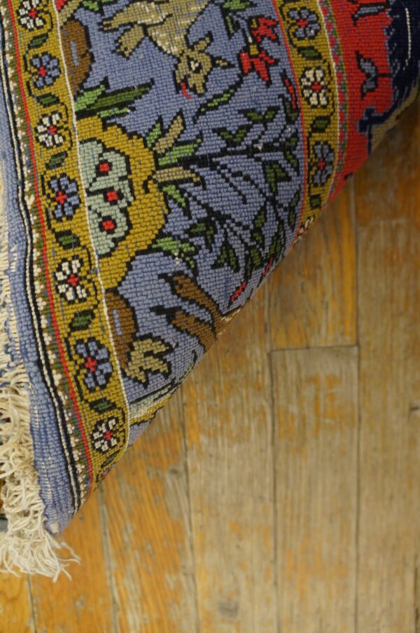 A rolled blue, gold, and red floral patterned rug rests diagonally on distressed wooden plank flooring.