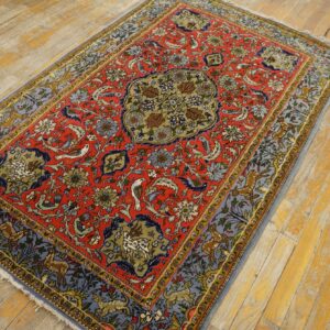 Red, blue, and gold patterned rug featuring animals, displayed on worn yellow wood flooring.