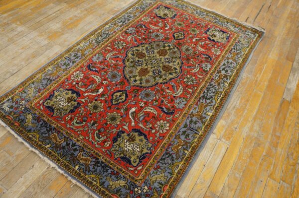 Red, blue, and gold patterned rug featuring animals, displayed on worn yellow wood flooring.