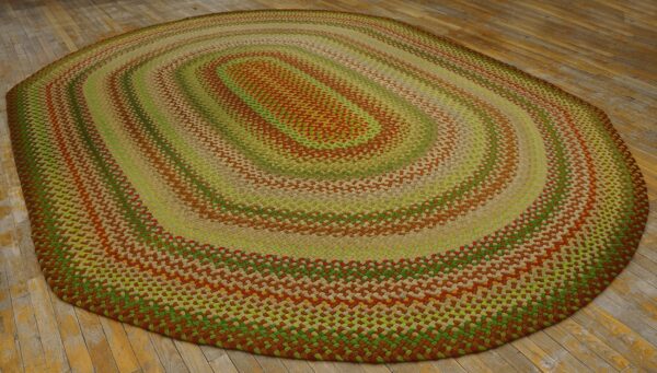 Braided oval rug with concentric rings of lime green, rust brown, and tan on aged wooden flooring.