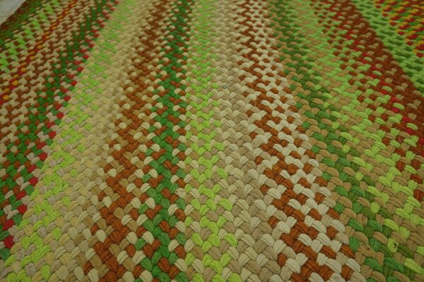 A tightly braided rug surface shows diagonal stripes in shades of green, beige, brown, and reddish tones.