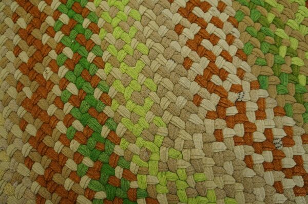Detailed close-up of a braided rug with color sections of rust orange, lime green, and natural tan.