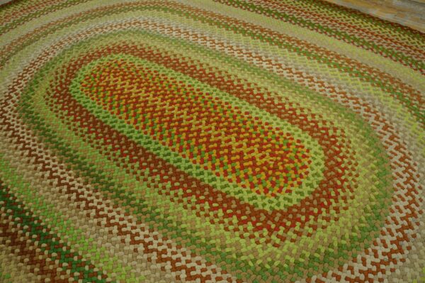 Braided oval rug featuring concentric bands of mixed red, yellow, green, and neutral earth tones.