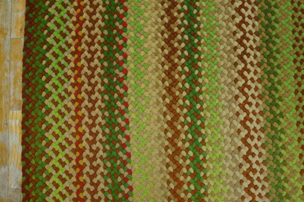 Textured braided rug in multicolored stripes of green, brown, and tan rests on distressed yellow wood floor.