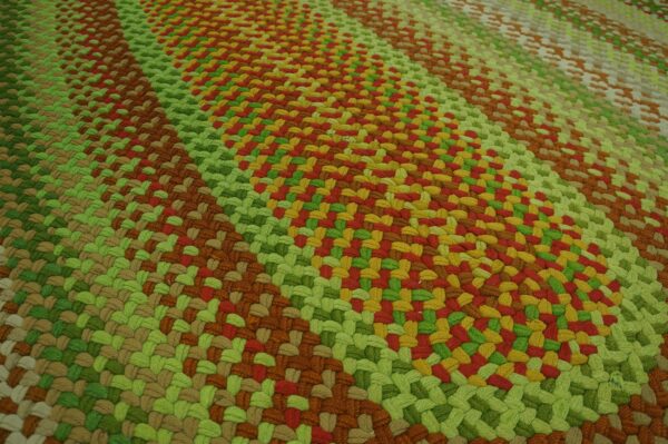 A high-textured, braided rug features diagonal bands of green, brown, red, and gold colors.