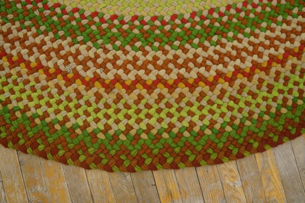 Braided rug featuring thick stripes of green, rust, beige, red, and yellow on distressed wooden floorboards.