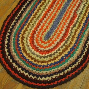 Multicolored braided rag rug, composed of concentric rows, rests on shiny golden-brown wood flooring.
