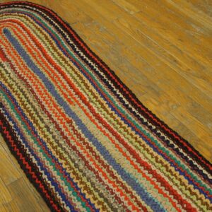 Multicolor oval braided runner rug featuring bands of red, blue, and orange sits on light brown wood flooring.