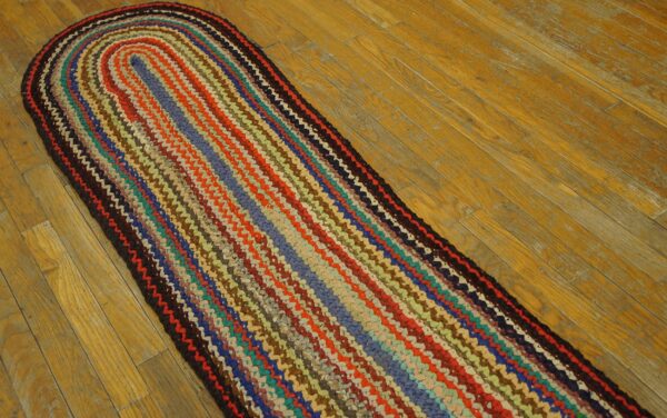 Multicolor oval braided runner rug featuring bands of red, blue, and orange sits on light brown wood flooring.