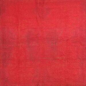 Red textile with raised quilting and faint gold thread highlights outlining floral and medallion patterns.