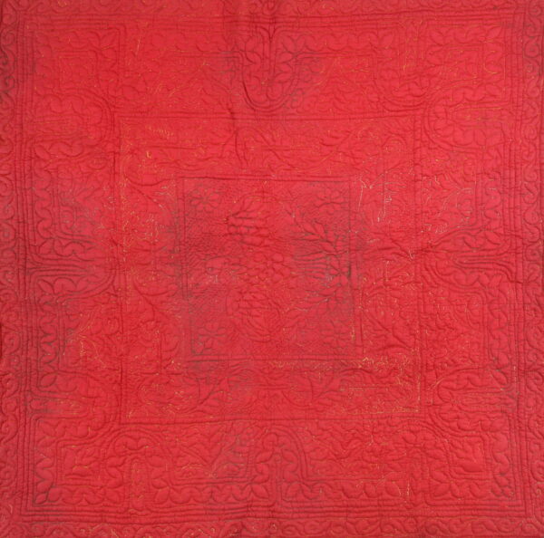 Red textile with raised quilting and faint gold thread highlights outlining floral and medallion patterns.