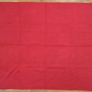 Red textured flat textile with organic quilted stitching rests on a light wood floor.