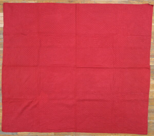 Red textured flat textile with organic quilted stitching rests on a light wood floor.