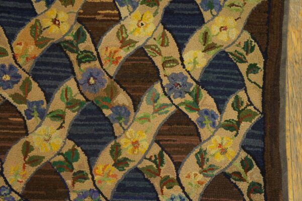 Textured hooked rug displays an interlocking floral trellis pattern in beige, yellow, blue, and dark brown colors.