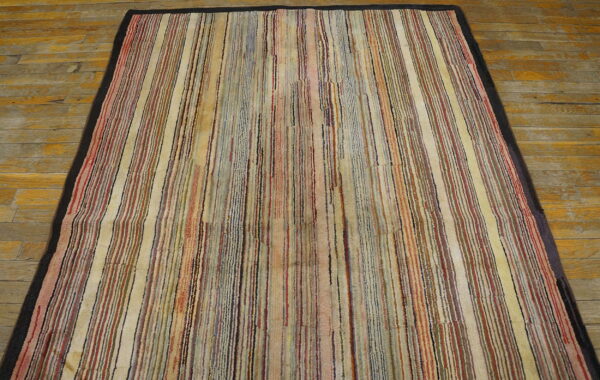 Muted, multi-color striped rug with a dark border rests on rustic wooden floorboards.