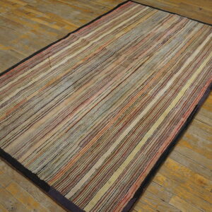 Earth-toned low-pile rug with narrow multicolored stripes and a dark border rests on distressed wooden planks.