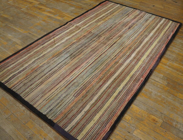 Earth-toned low-pile rug with narrow multicolored stripes and a dark border rests on distressed wooden planks.