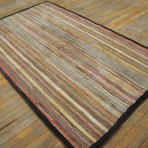 Low-pile rug with thin multicolor stripes and a dark border displayed on distressed wood planks.